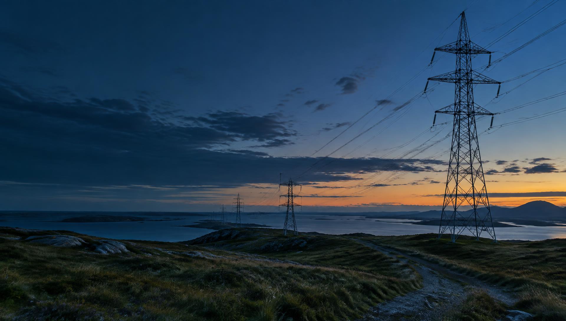 Illustrative image: electricity transmission lines crossing a coastal landscape at dusk